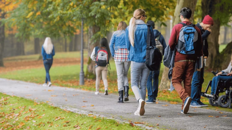 Grupo de estudiantes con mochilas paseando por un parque en otoño