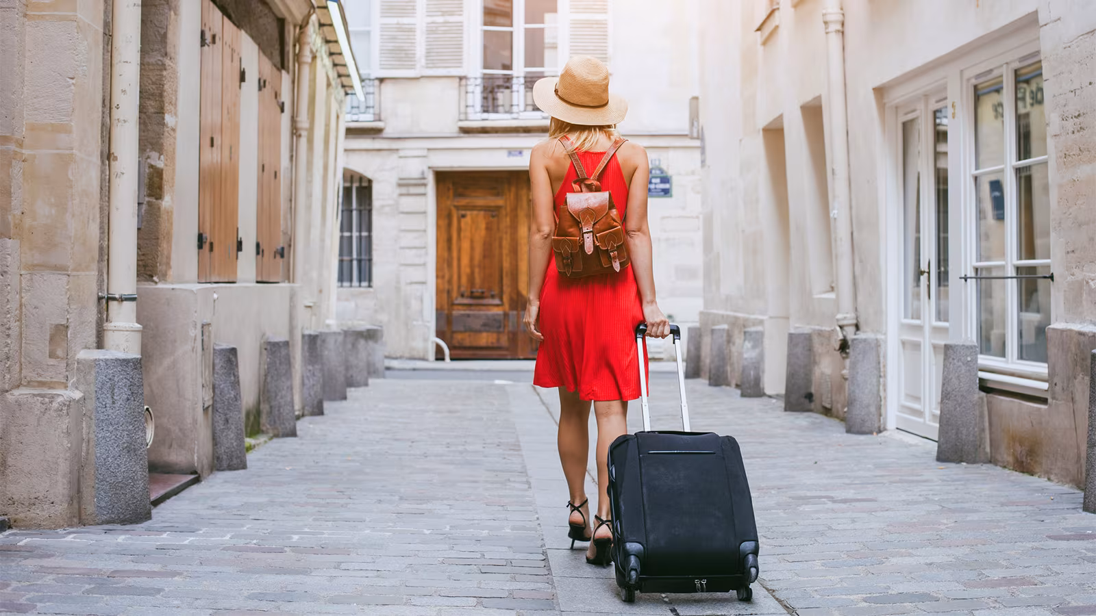 Viajera con vestido rojo y maleta caminando por una calle empedrada